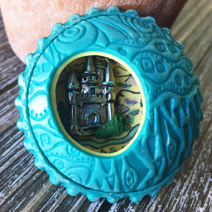 a round lentil shaped hollow bead with an oval cut out and a castle inside