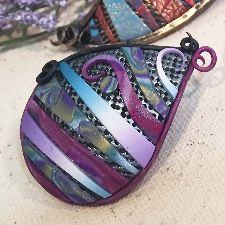 polymer clay pendant with layers of textures and veneer sheets in shades of purple, turquoise and silver