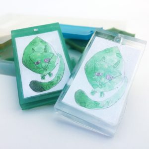 A child's drawing of a green cat preserved in clear resin as a pendant, keychain or jewelry.