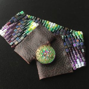 A beaded bracelet in greens and purples with a leather and button closure.