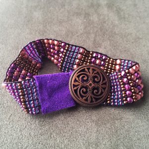A beaded bracelet in shades of purple with a leather and button closure.