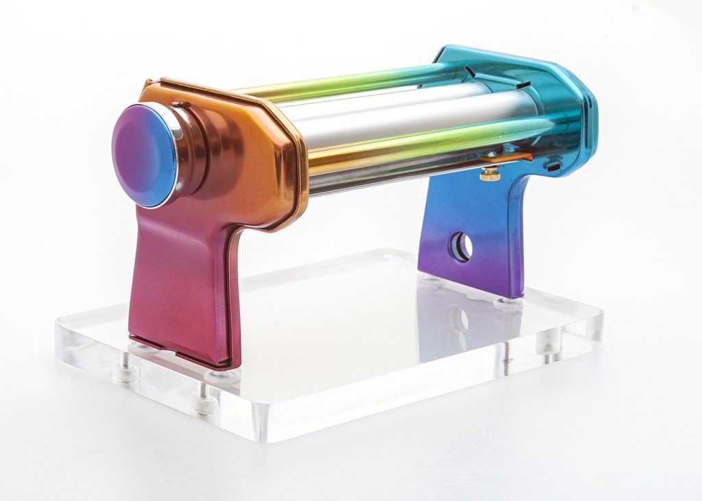 A pasta machine painted in rainbow colors on an acrylic base